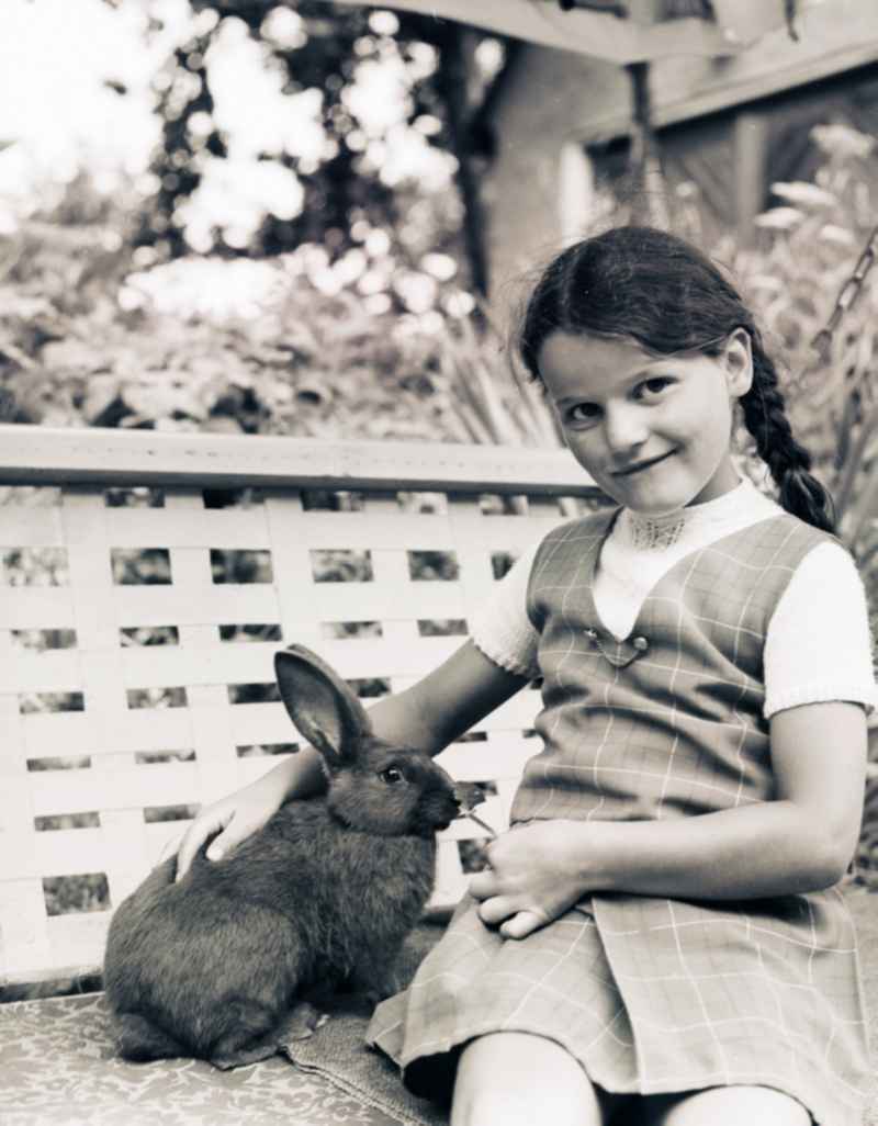 Girl sits with a rabbit of a garden swing in Scheibenberg in the federal state Saxony in the area of the former GDR, German democratic republic