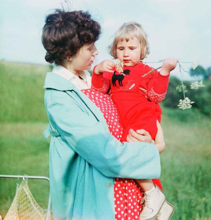 A mother has her toddler on the arm with a walk in a park in Schlettau in the federal state Saxony in the area of the former GDR, German democratic republic