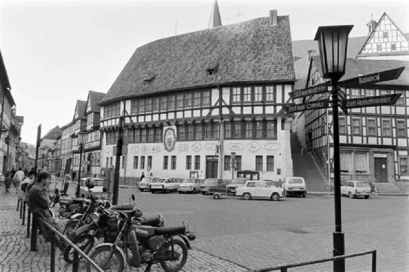 The town hall of Stolberg (Harz) in the southern Harz region in the federal state of Saxony-Anhalt on the territory of the former GDR, German Democratic Republic. Model Simson motorbikes and cars are parked on the street. A signpost shows the direction to the FDGB recreation home ' Comenius ' and ' Waldfrieden '