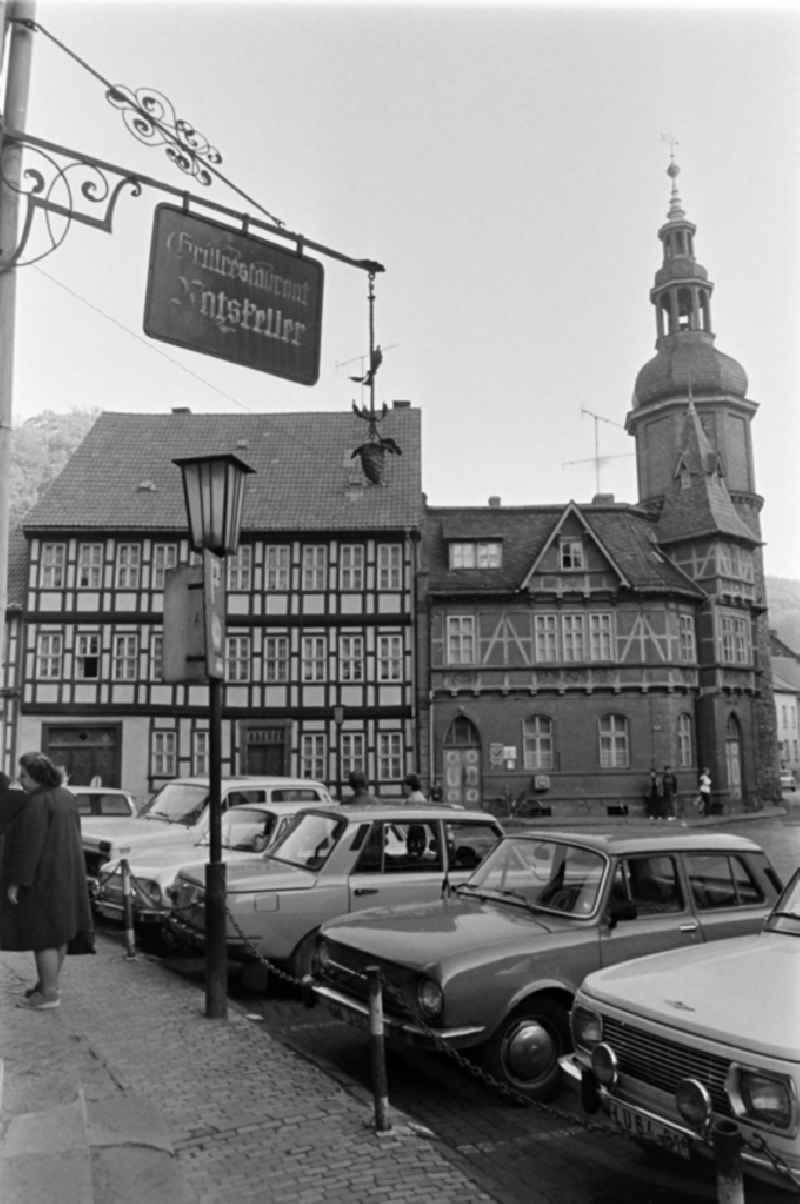 Cars parked at the corner of Markt and Rittergasse, in the background the Seigerturm in Stolberg (Harz) in the southern Harz region in the federal state of Saxony-Anhalt in the territory of the former GDR, German Democratic Republic. A sign with the inscription ' Grillrestaurant Ratskeller ' rises above the pavement