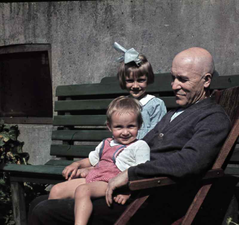 Kinder sitzen beim Großvater im Garten. Childrens sitting by the grandfather in the garden.
