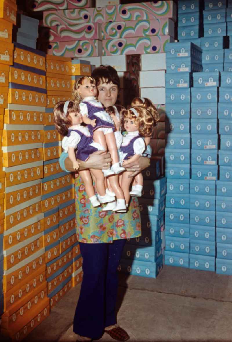 Eine Mitarbeiterin des VEB Kombinat Spielwaren Sonneberg 'sonni' präsentiert fertige Puppen auf ihrem Arm, im Hintergrund stapeln sich die Verkaufskartons. Die Sonneberger Puppen waren nicht nur in der DDR beliebt, sondern trugen den Namen der Stadt in alle Welt.