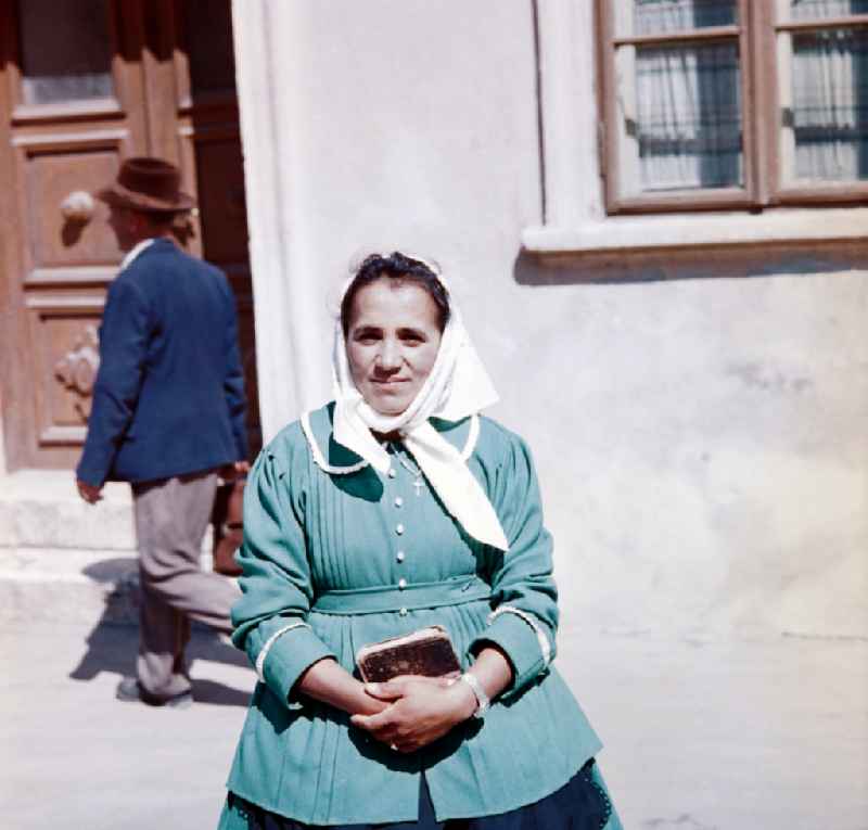 A woman is standing with a book in her hands in front of a house in the former CSSR while she is being photographed