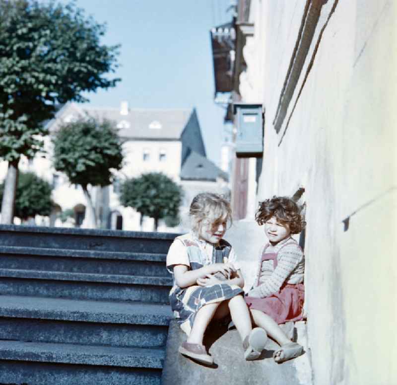Two children are sitting on a staircase in a city of the former CSSR