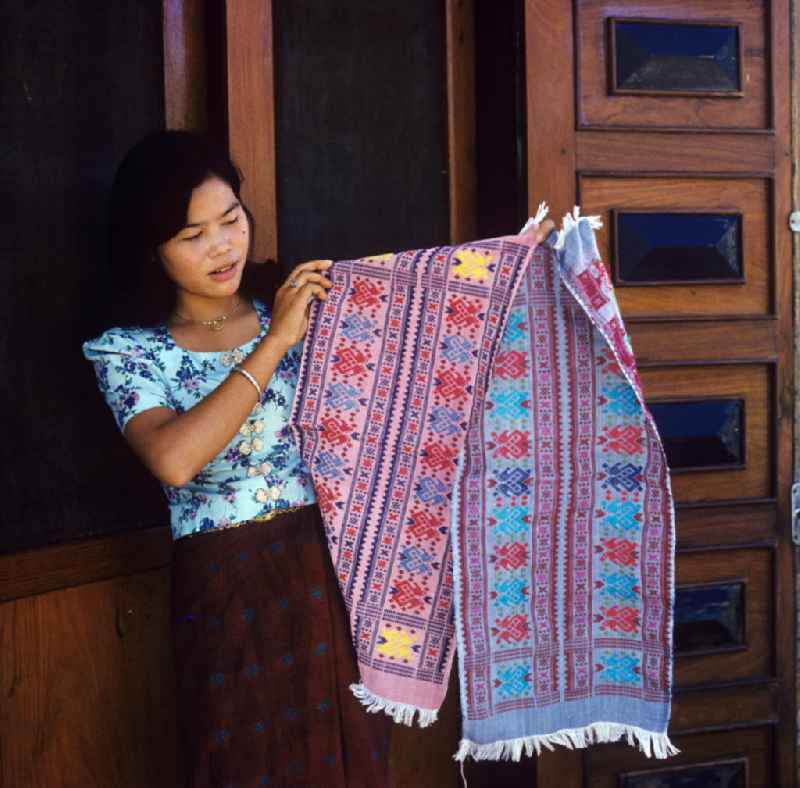 Eine Frau präsentiert zwei Teppiche aus einer Weberei in Vientiane, der Hauptstadt der Demokratischen Volksrepublik Laos.
