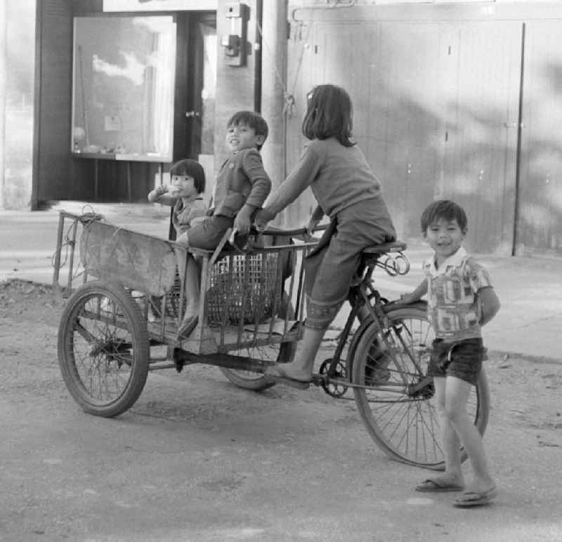 Kinder fahren auf einem Fahrrad mit drei Rädern auf einer Straße in Vientiane, der Hauptstadt der Demokratischen Volksrepublik Laos.