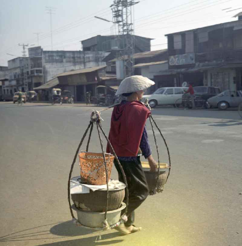 Eine Frau trägt Schüsseln und geschulterte Körbe in Vientiane, der Hauptstadt der Demokratischen Volksrepublik Laos.