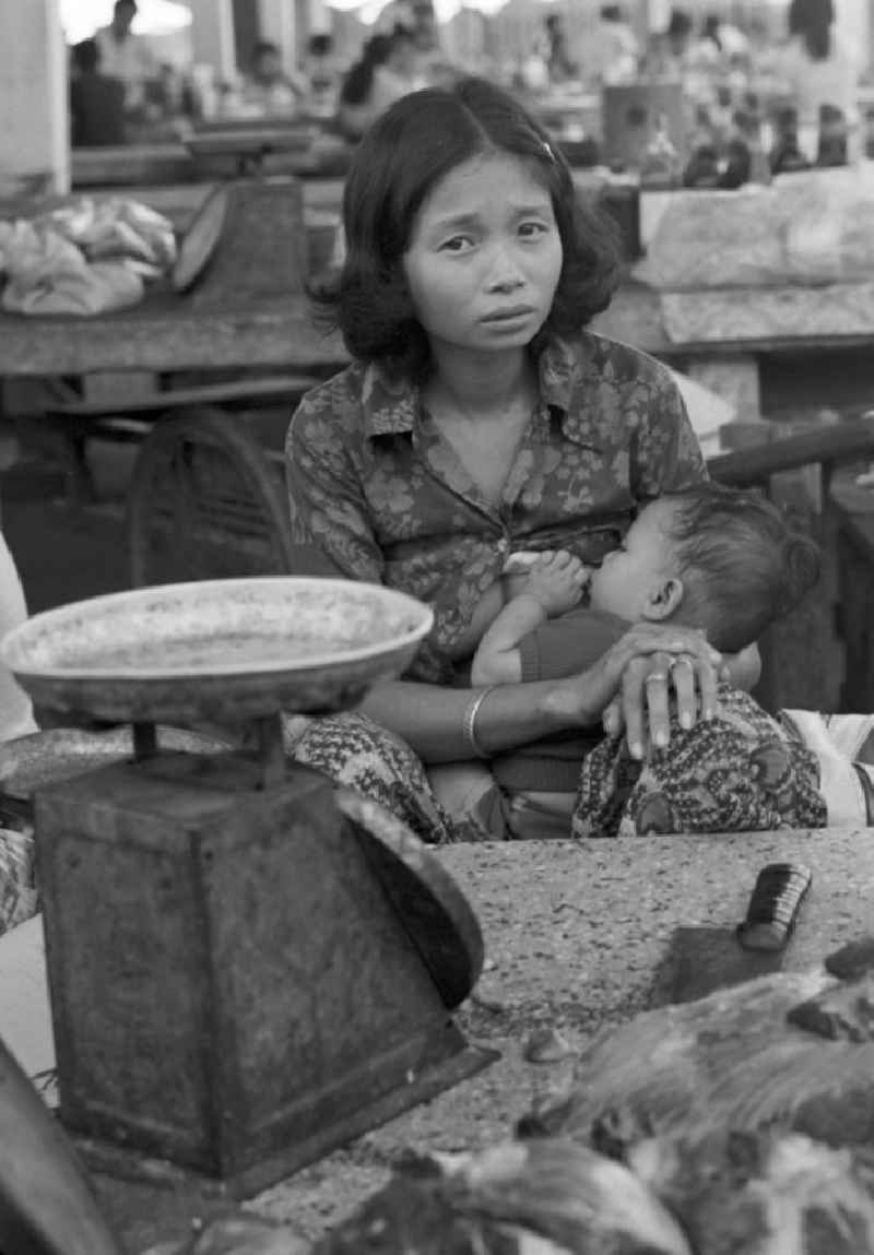 Marktszene in Vientiane, der Hauptstadt der Demokratischen Volksrepublik Laos - eine Frau am Verkaufsstand beim Stillen ihres Babys.