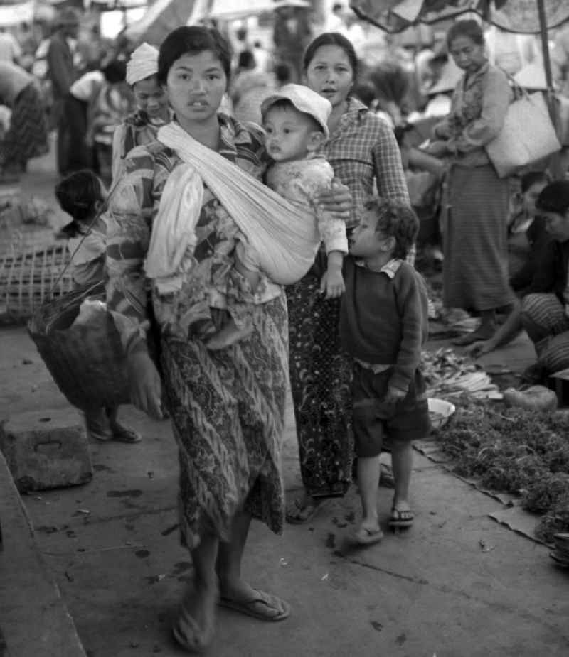 Eine Frau trägt ihr Baby in einem Tragetuch über den Markt in Vientiane, der Hauptstadt der Demokratischen Volksrepublik Laos.