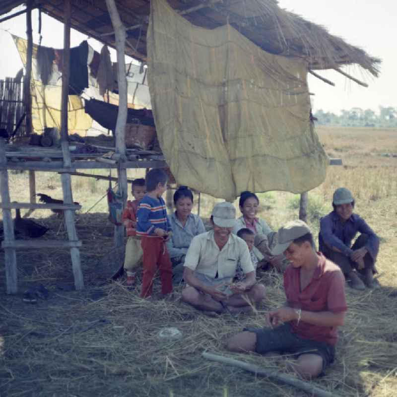 Männer, Frauen und Kinder sitzen während der Reisernte im Schatten einer Hütte auf einem Feld in der Demokratischen Volksrepublik Laos.
