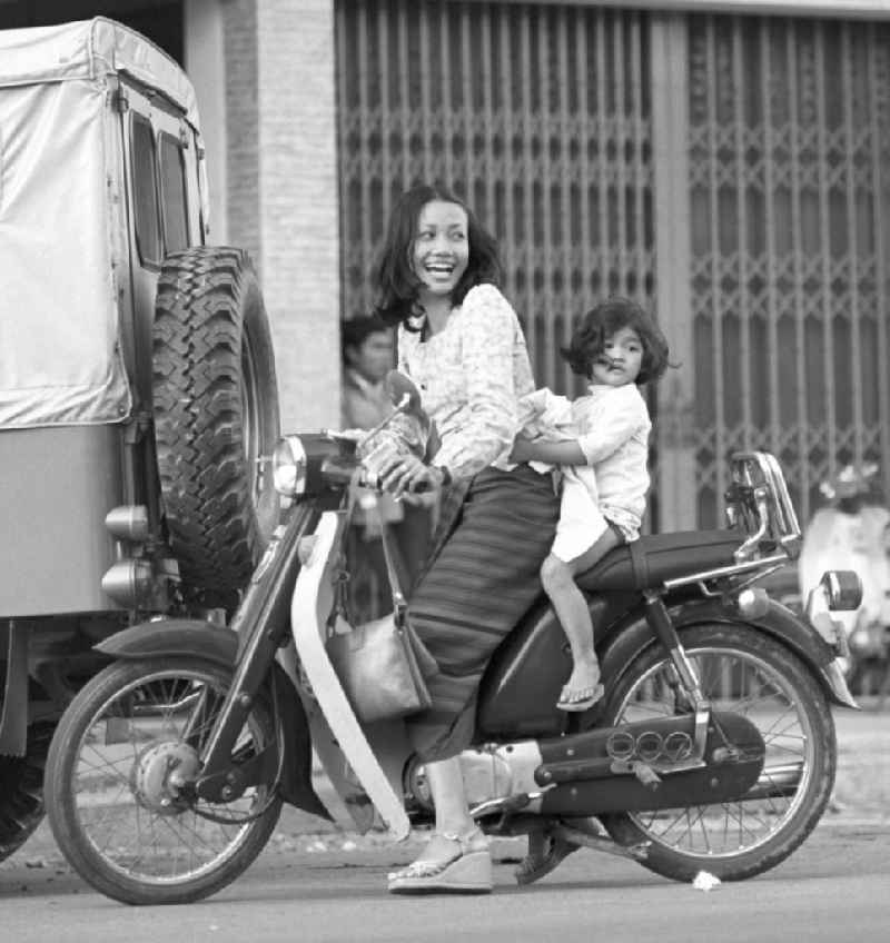 Eine Frau fährt mit ihrem Kind auf einem Moped auf einer Straße in Vientiane, der Hauptstadt der Demokratischen Volksrepublik Laos.