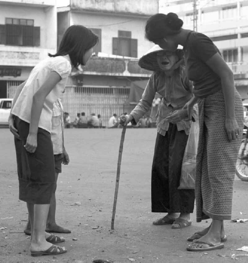 Zwei junge Frauen kümmern sich um eine Greisin auf einer Straße in Vientiane, der Hauptstadt der Demokratischen Volksrepublik Laos.