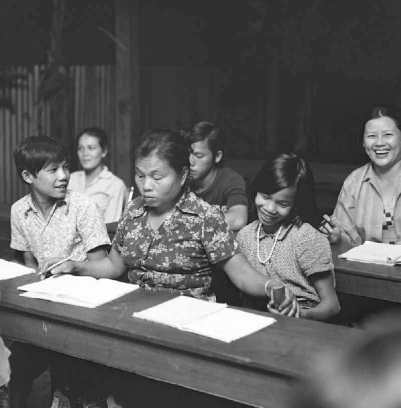 Seite an Seite lernen junge und erwachsene Laoten in einer Schule schreiben und lesen. Nach der Gründung der Volksrepublik Laos im Dezember 1975 wurde das Schulsystem von der neuen kommunistischen Regierung in Laos wieder aufgebaut, um dem in der Bevölkerung weit verbreiteten Analphabetismus entgegenzuwirken.