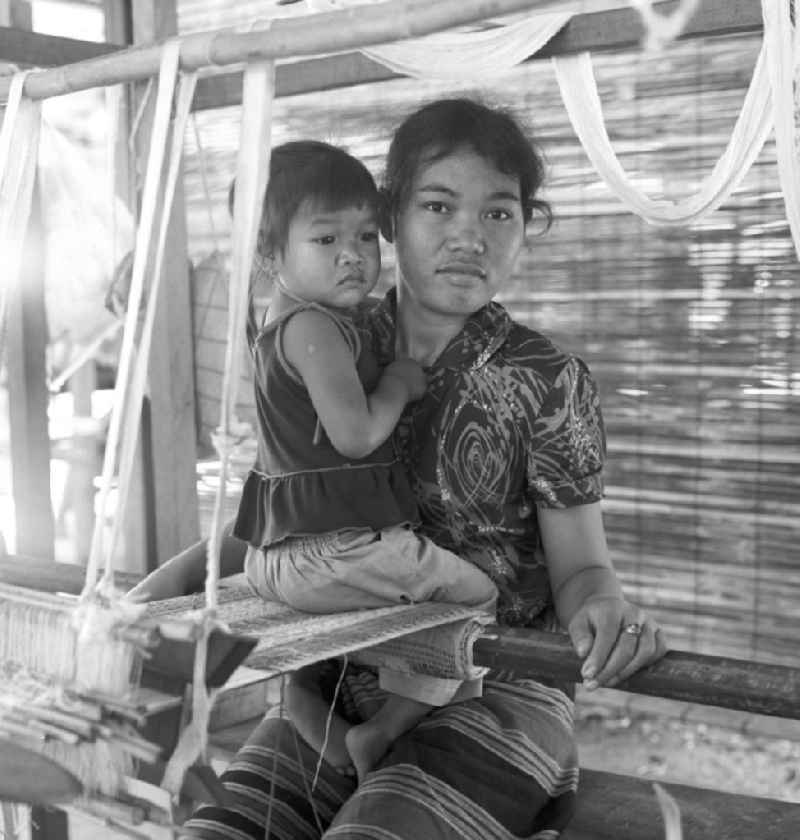Eine Frau mit ihrem kleinen Kind an einem Holzwebstuhl in einer Weberei in Vientiane, der Hauptstadt der Demokratischen Volksrepublik Laos.