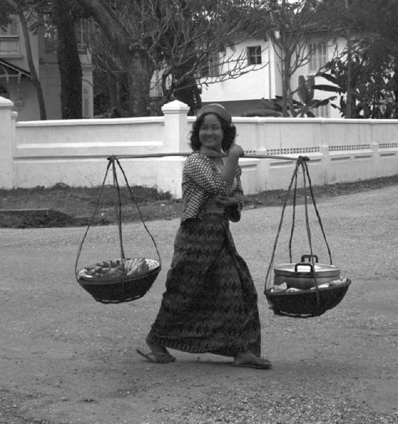 Eine junge Frau läuft mit geschulterten Körben auf einer Straße in Vientiane in der Demokratischen Volksrepublik Laos.