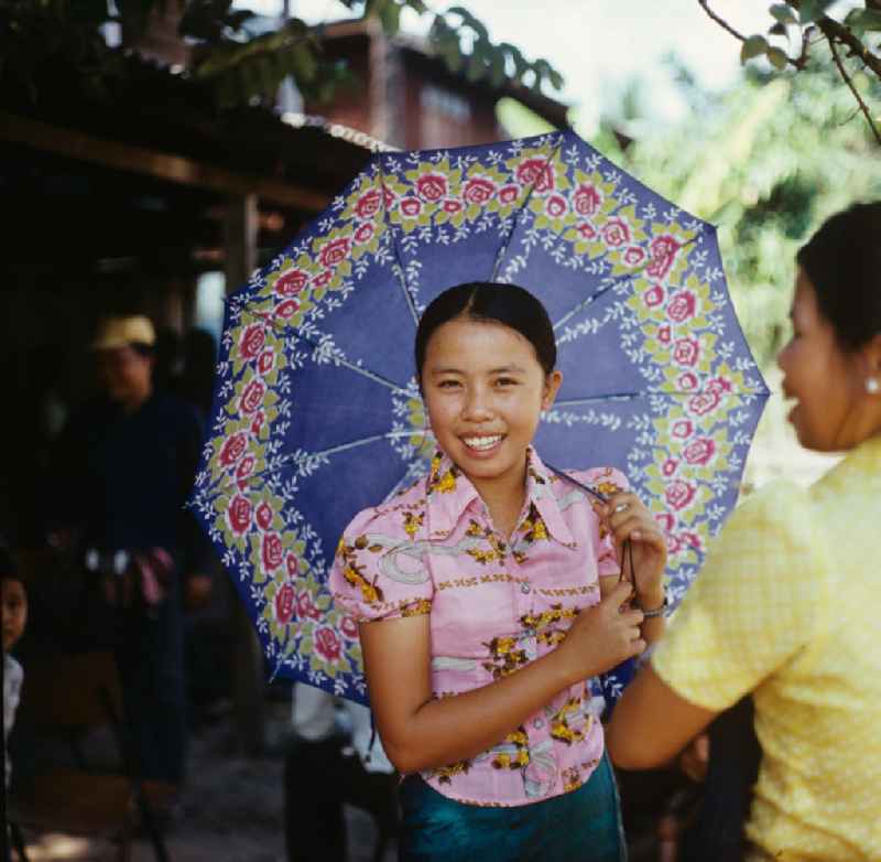 Junges Mädchen mit Schirm auf einer Hochzeitsfeier in einem Dorf in der Demokratischen Volksrepublik Laos.