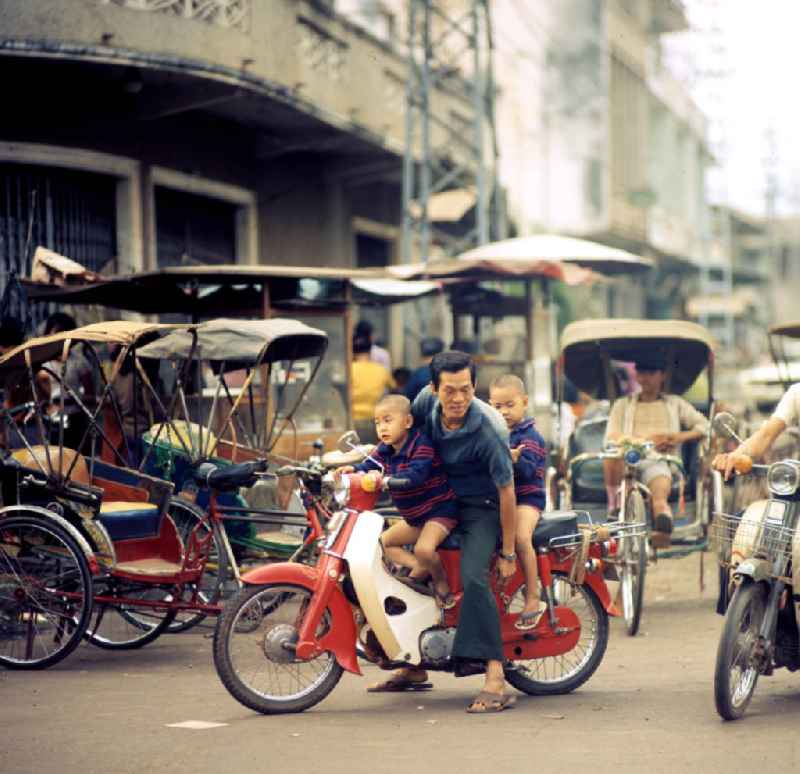 Ein Mann mit seinen Kindern auf einem Motorrad in Vientiane in der Demokratischen Volksrepublik Laos.