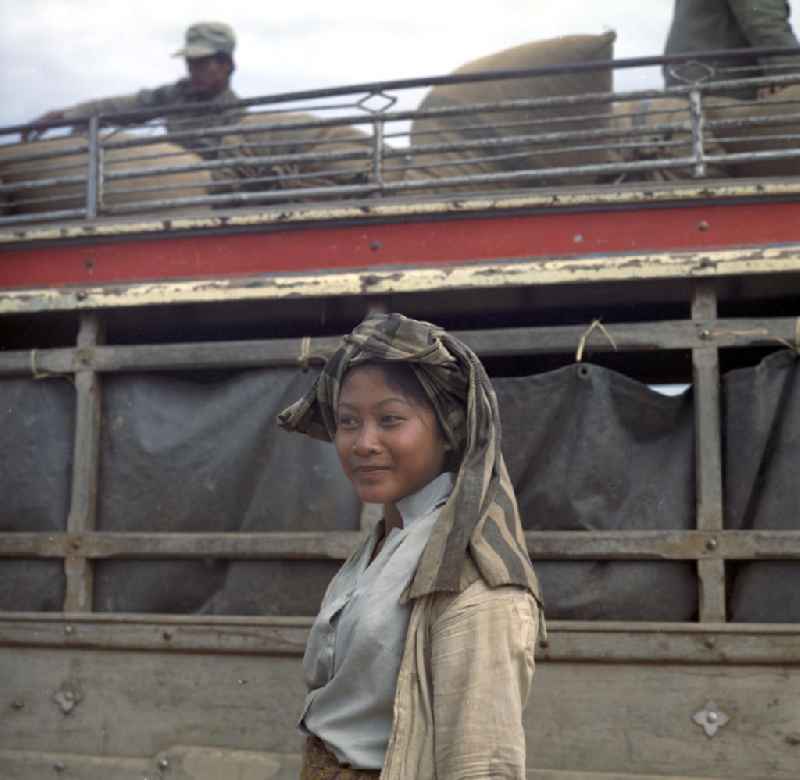 Frau vor einem Bus mit Reissäcken in der Demokratischen Volksrepublik Laos.