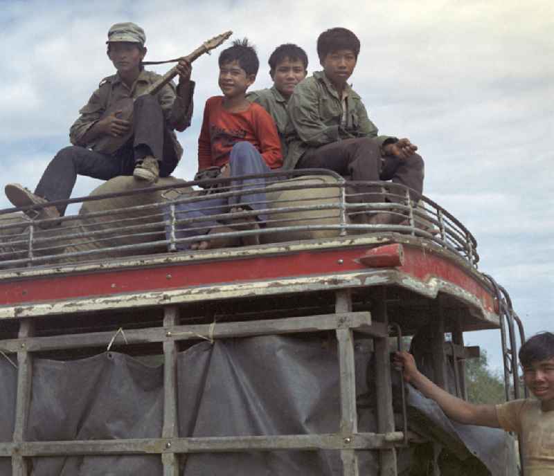 Junge Männer und ein Lautenspieler sitzen auf dem Dach eines Transporters in der Demokratischen Volksrepublik Laos.