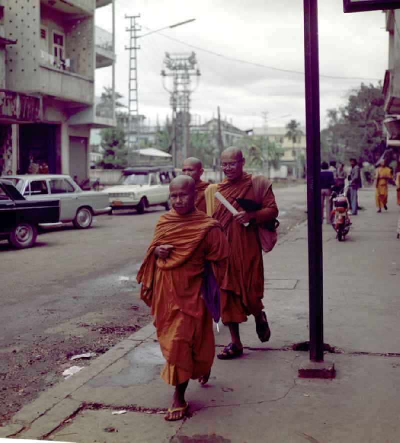Bettelmönche auf einer Straße in Vientiane in der Demokratischen Volksrepublik Laos, aufgenommen am 4.1.1977. Bis zur Ausrufung der Volksrepublik Laos am 2. Dezember 1975 bestimmte der Theravada-Buddhismus die kulturelle Entwicklung im Land. Nachdem die anfängliche Unterdrückung der traditionellen buddhistischen Bräuche durch die neuen kommunistischen Machthaber mißlang, fand Laos in den folgenden Jahrzehnten einen eigenen Weg der Koexistenz von Buddhismus und Sozialismus.