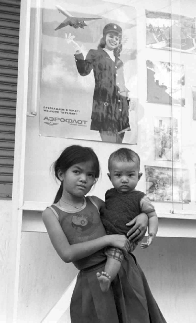 Ein Mädchen steht mit einem Baby auf dem Arm vor einem Werbeplakat der russischen Fluggesellschaft Aeroflot in Vientiane in der Demokratischen Volksrepublik Laos.