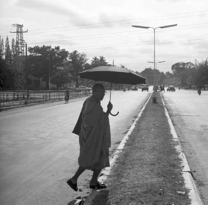 Ein Mönch mit Schirm läuft über eine Straße in Vientiane in der Demokratischen Volksrepublik Laos.