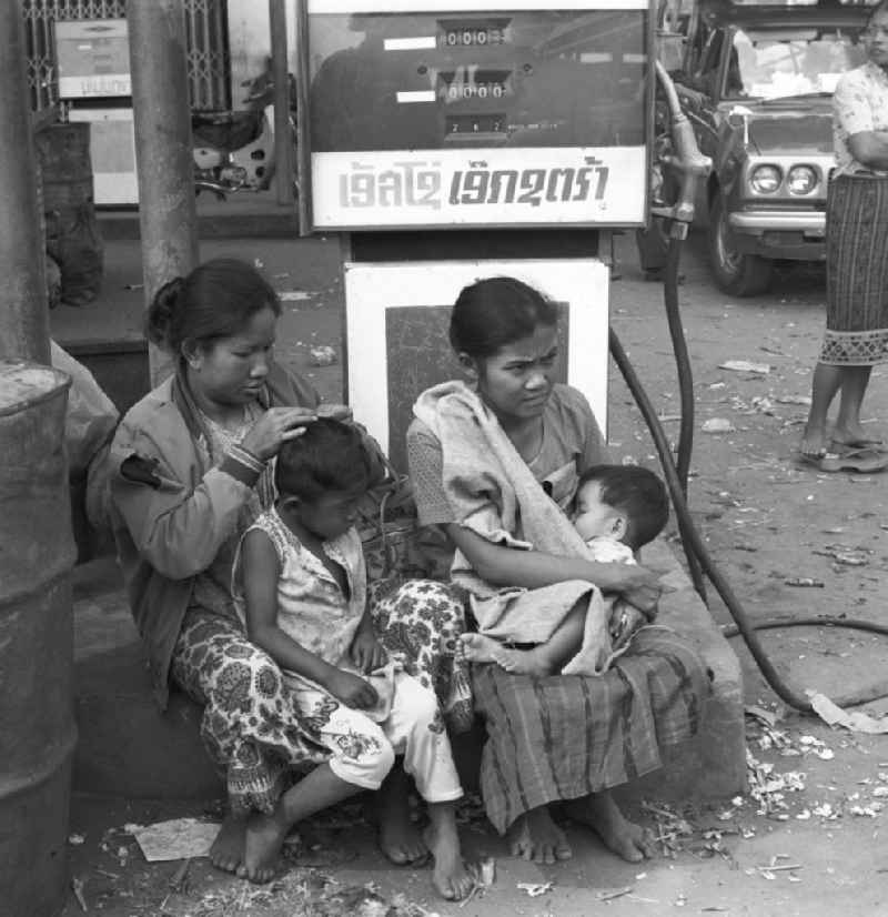Frauen sitzen mit ihren Kindern vor der Zapfsäule einer Tankstelle in Vientiane in der Demokratischen Volksrepublik Laos.