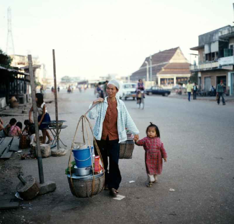 Frau mit geschulterten Körben und Kind an der Hand auf einer Straße in Vientiane in der Demokratischen Volksrepublik Laos.