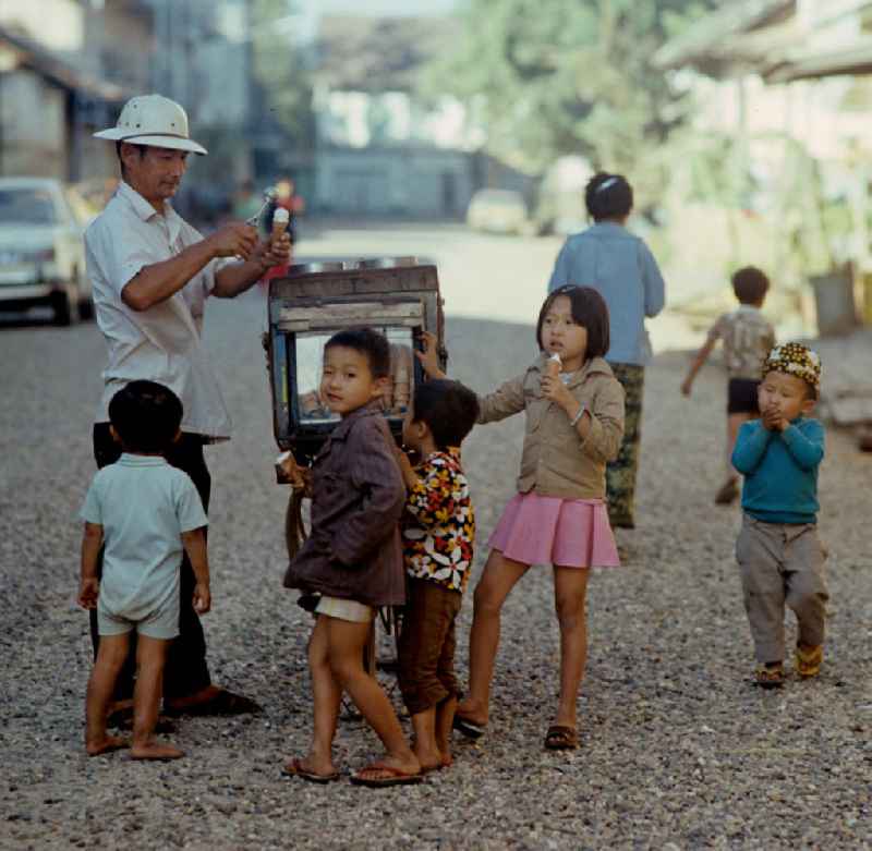 Kinder kaufen sich an einem kleinen Eiswagen auf einer Straße in Vientiane in der Demokratischen Volksrepublik Laos ein Eis.