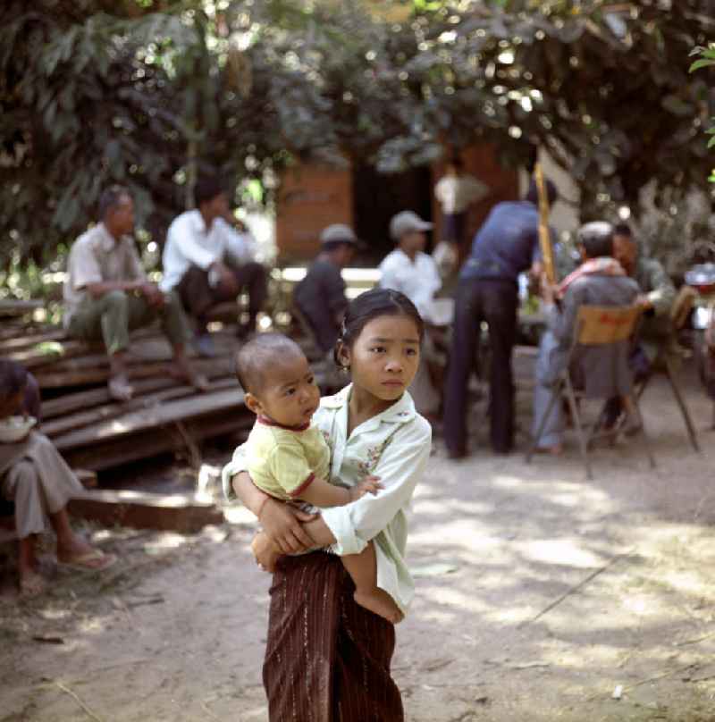 Ein Mädchen mit Baby auf dem Arm während einer Hochzeit in einem Dorf in der Demokratischen Volksrepublik Laos.