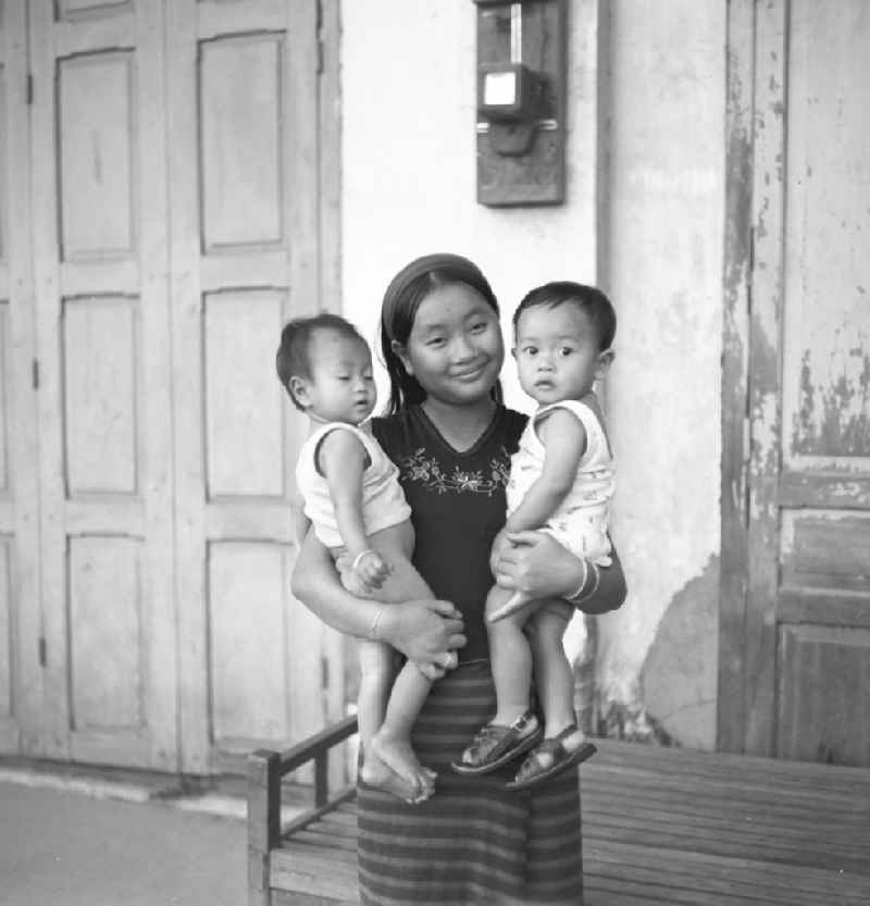 Mädchen mit zwei Kindern auf dem Arm in einem Haus in Vientiane in der Demokratischen Volksrepublik Laos.
