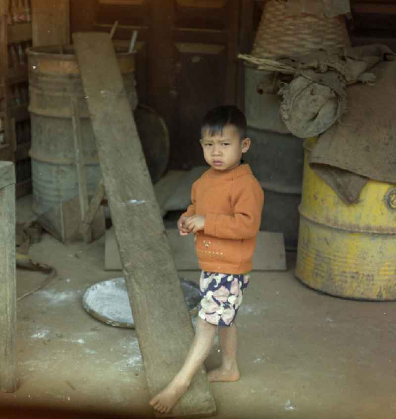 Junge vor einer Hütte an einer Straße in der Demokratischen Volksrepublik Laos.