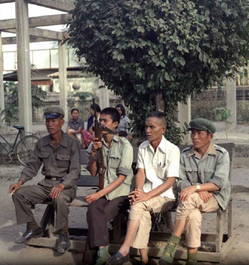 Milizionäre sitzen auf einer Bank in Vientiane in der Demokratischen Volksrepublik Laos.