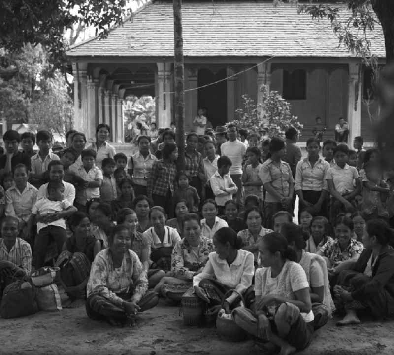 Ein feierlicher Empfang erwartet die  'umerzogenen' Rückkehrer von der Frauen- und Männerinsel in Vientiane in der Demokratischen Volksrepublik Laos. Das Nam Ngum Reservoir entstand mit der Fertigstellung des gleichnamigen Staudamms im Jahr 1971. Die im See liegenden Inseln dienten in den 7