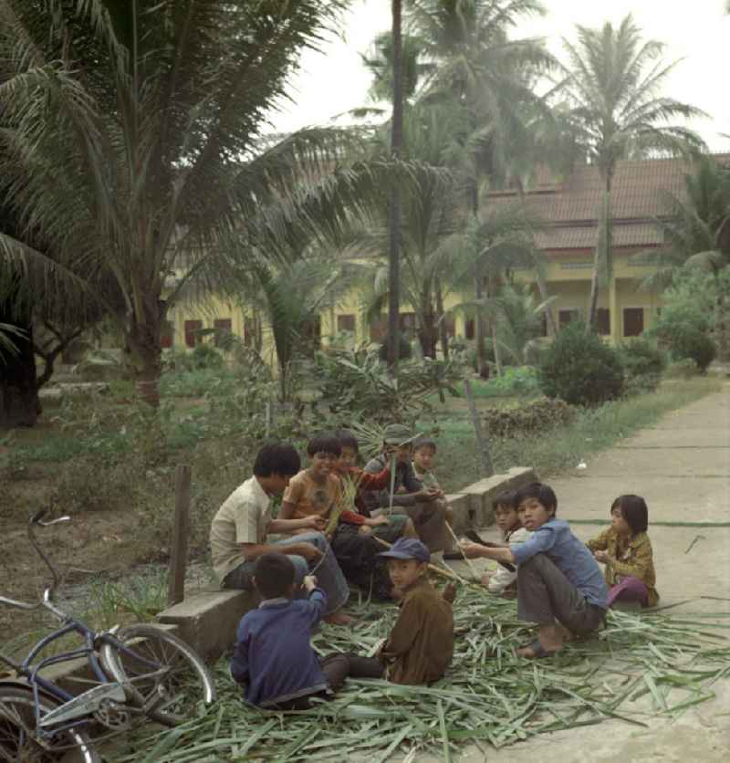 Kinder basteln 'Flöten' aus den Blättern einer Palme in Vientiane in der Demokratischen Volksrepublik Laos.