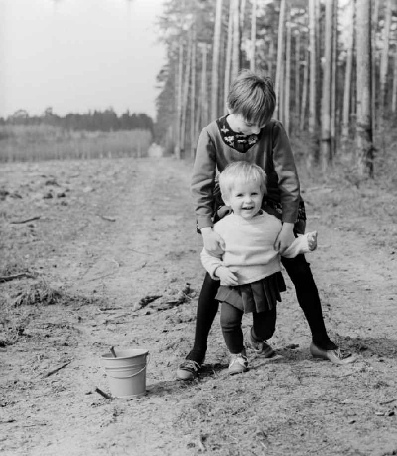 Two small children with a bucket and a shovel play in the sand in Wernigerode in the federal state Saxony-Anhalt on the territory of the former GDR, German Democratic Republic