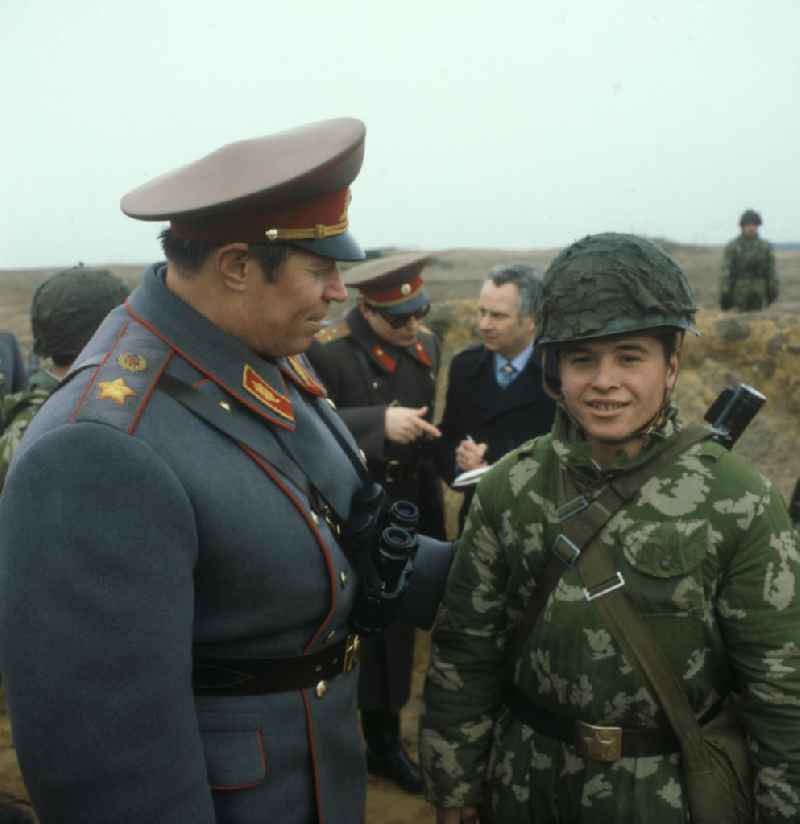 Armeegeneral Michail Saizew, Oberkommandierender der Gruppe der Sowjetischen Streitkräfte in Deutschland, mit Soldat in Tarnanzug beim Manöver in Wolmirstedt. Soldaten und Offiziere im Hintergrund.