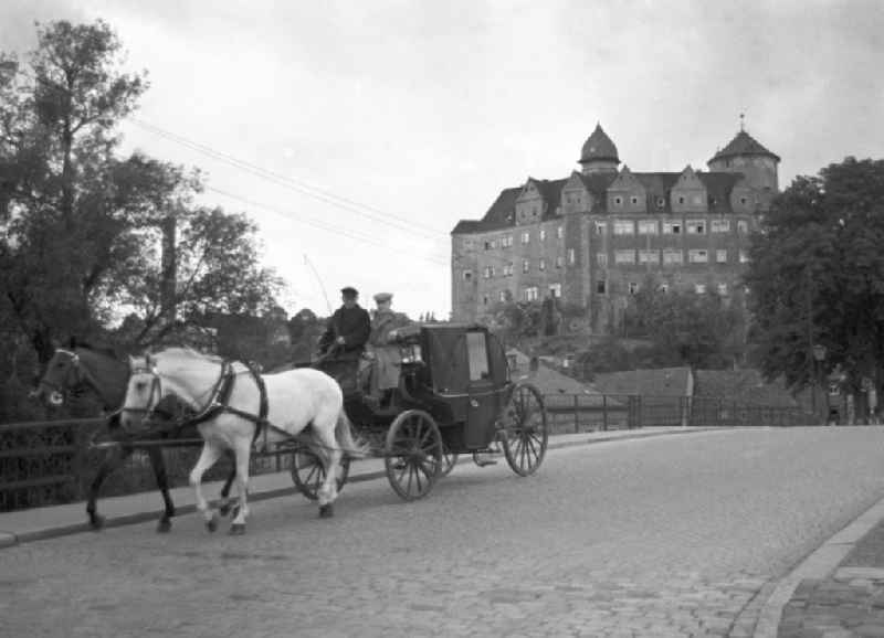 Ein Kutsche mit Zweigespann fährt auf einer Straße in Zschopau, mit Blick auf das Schloss Wildeck im Hintergrund.