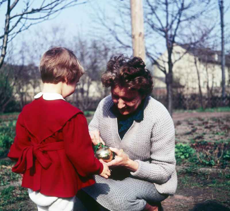 A small child in a red dress with the Easter egg look in the garden in Zschopau in the federal state Saxony in the area of the former GDR, German democratic republic